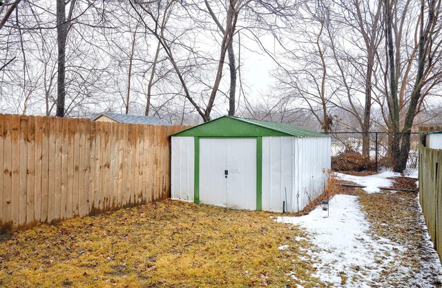 snow covered structure featuring an outbuilding, a storage unit, and a fenced backyard