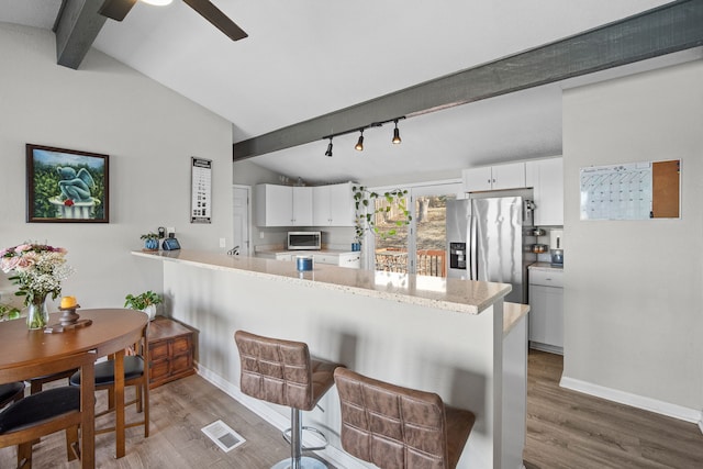 kitchen featuring a peninsula, white cabinets, vaulted ceiling with beams, and appliances with stainless steel finishes