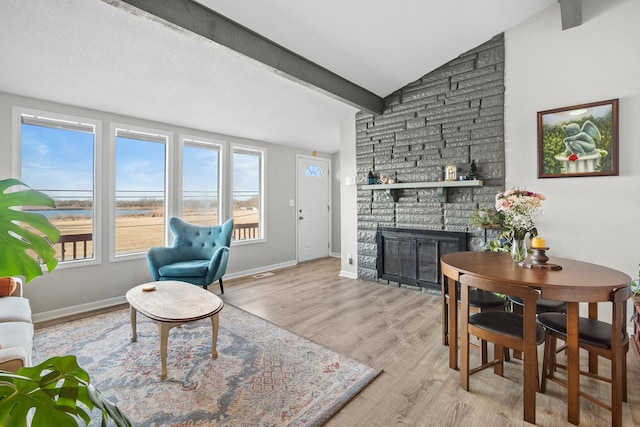 living area featuring wood finished floors, lofted ceiling with beams, a fireplace, and baseboards