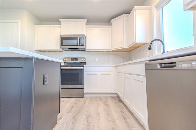 kitchen featuring light wood-type flooring, tasteful backsplash, white cabinetry, appliances with stainless steel finishes, and light countertops