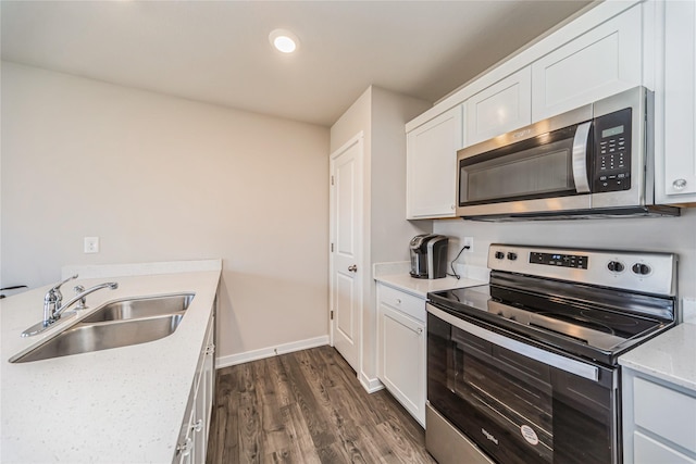 kitchen with dark wood-type flooring, baseboards, white cabinets, stainless steel appliances, and a sink