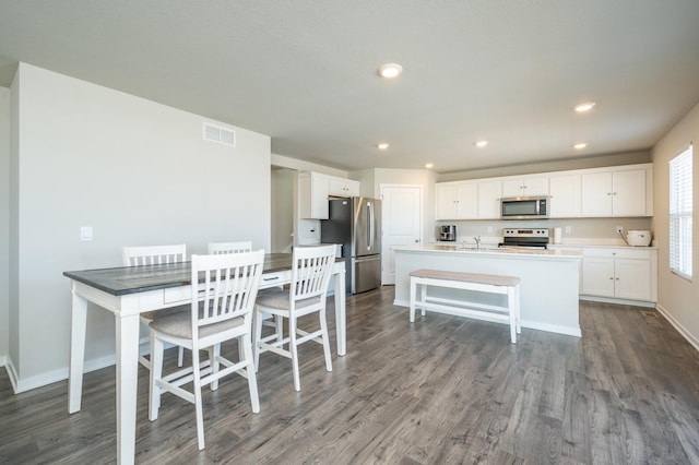 kitchen featuring baseboards, a center island with sink, dark wood-style flooring, stainless steel appliances, and white cabinetry