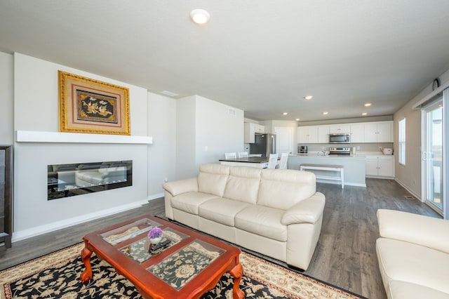 living area featuring a glass covered fireplace, recessed lighting, dark wood-style floors, and baseboards