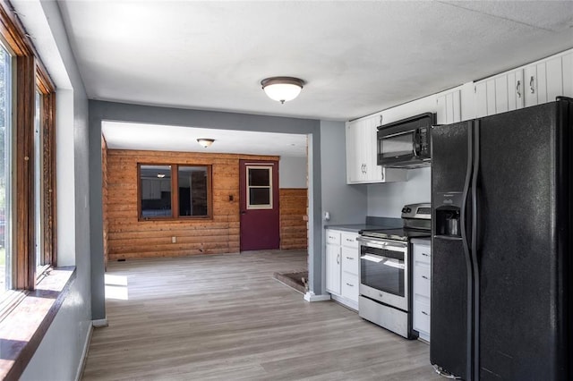 kitchen featuring wooden walls, black appliances, open floor plan, light wood-type flooring, and white cabinetry