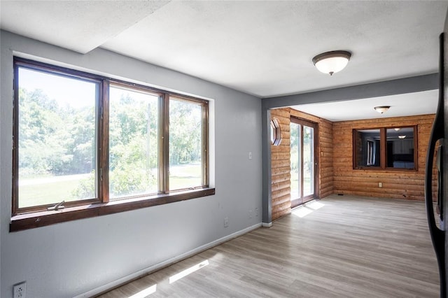 spare room with log walls, baseboards, a textured ceiling, and light wood finished floors