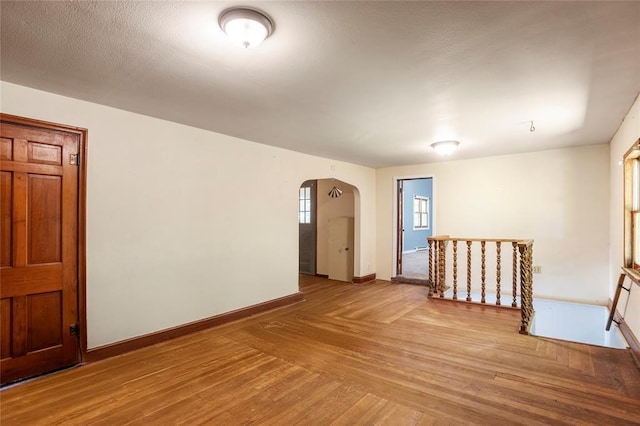 spare room featuring arched walkways, parquet floors, and baseboards