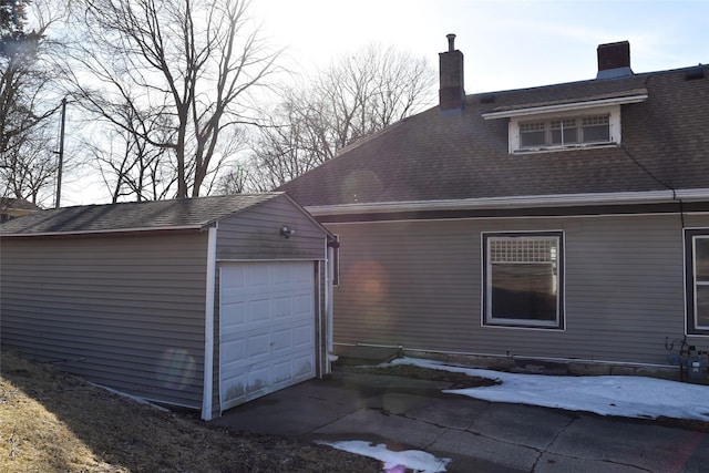 view of side of home featuring driveway, a shingled roof, a chimney, an outdoor structure, and a garage