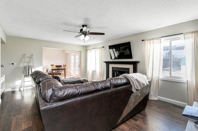 living room with a tiled fireplace, a wealth of natural light, visible vents, and dark wood-style flooring