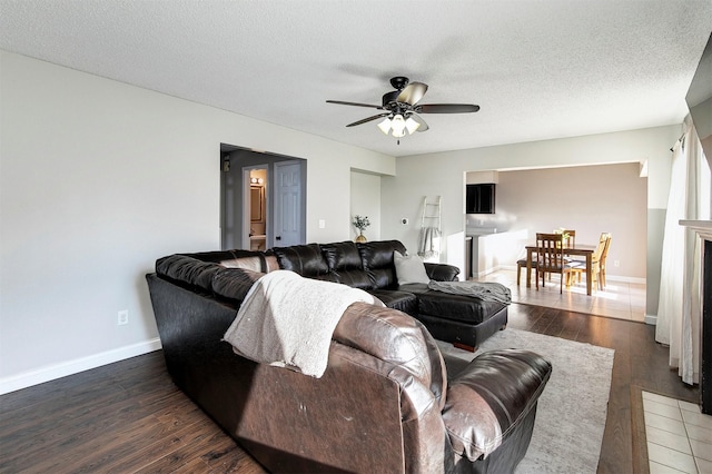 living area with baseboards, a textured ceiling, dark wood finished floors, and a ceiling fan