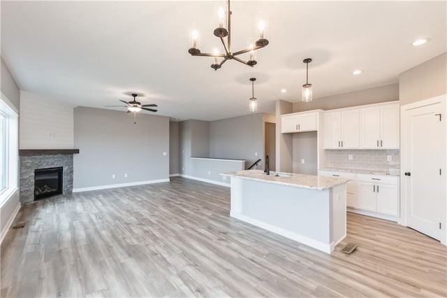 kitchen with decorative backsplash, white cabinets, ceiling fan with notable chandelier, and light wood-style flooring