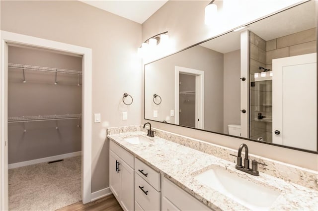 bathroom with double vanity, toilet, a tile shower, and a sink