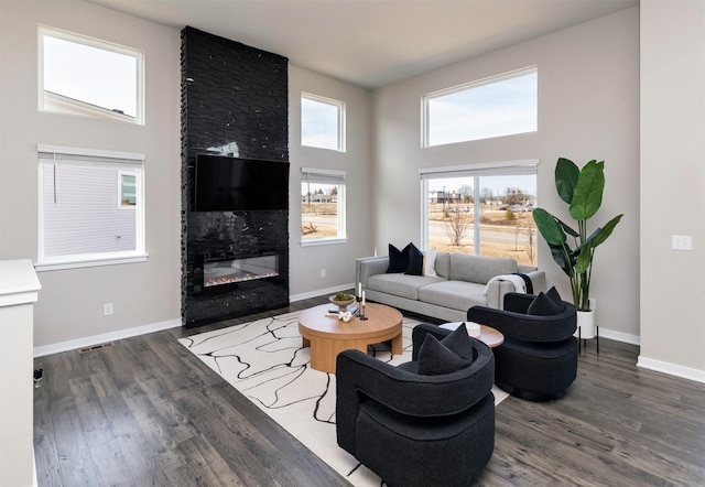 living room with baseboards, a large fireplace, a high ceiling, and wood finished floors