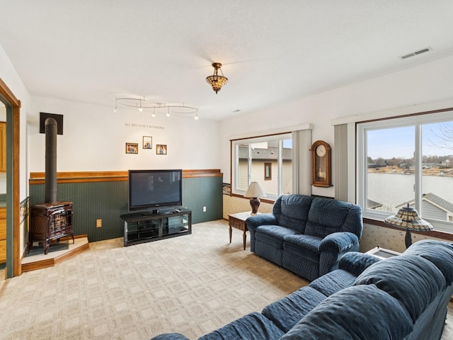 carpeted living room featuring visible vents, a wood stove, and a wainscoted wall