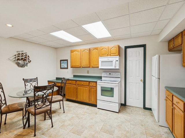 kitchen with white appliances, brown cabinets, and a drop ceiling