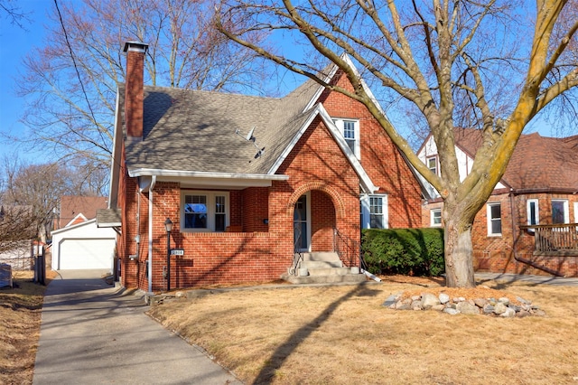 tudor house featuring an outbuilding, roof with shingles, a garage, brick siding, and a chimney