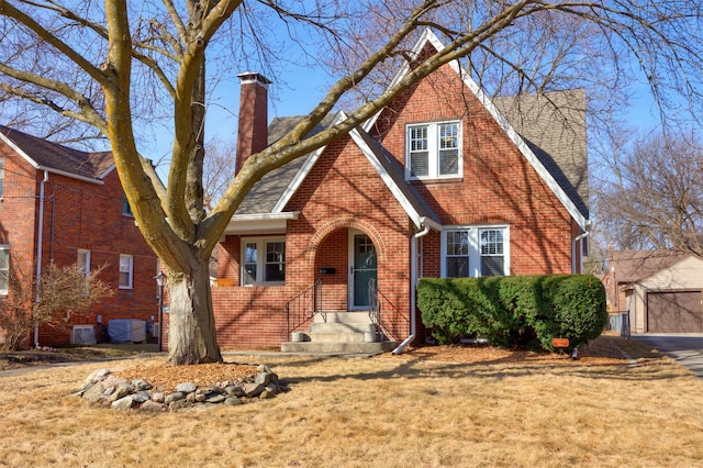 view of front of house with an outdoor structure, a front yard, a shingled roof, brick siding, and a chimney