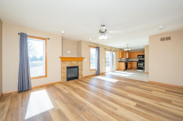 unfurnished living room with visible vents, light wood-style flooring, ceiling fan with notable chandelier, baseboards, and a tile fireplace