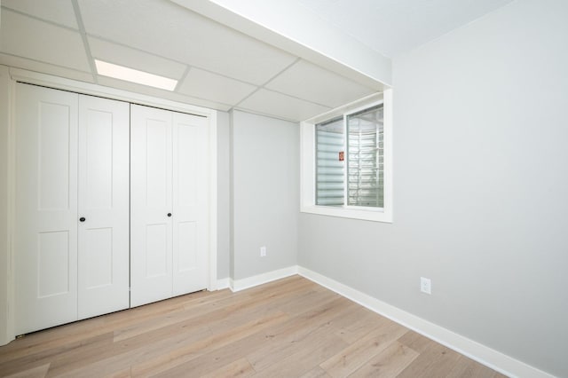 unfurnished bedroom with a closet, baseboards, a paneled ceiling, and light wood-style floors