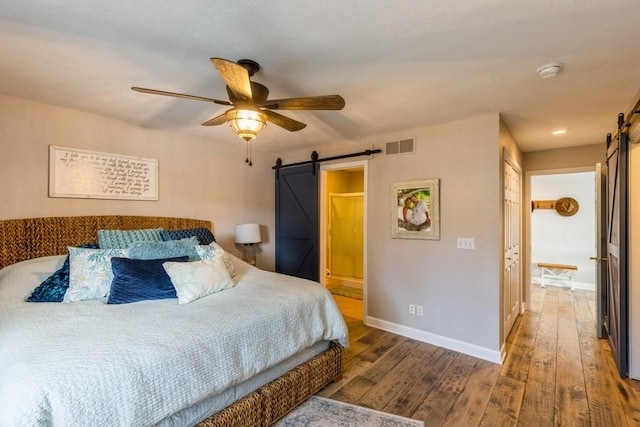 bedroom with visible vents, ensuite bathroom, hardwood / wood-style flooring, a barn door, and baseboards