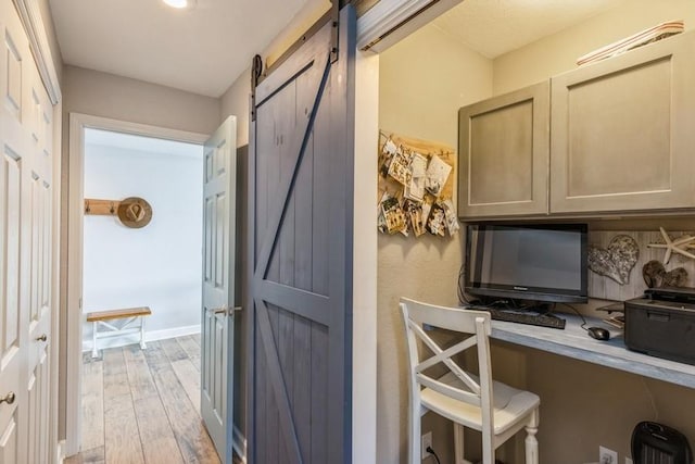 office area featuring a barn door, baseboards, light wood finished floors, and built in study area