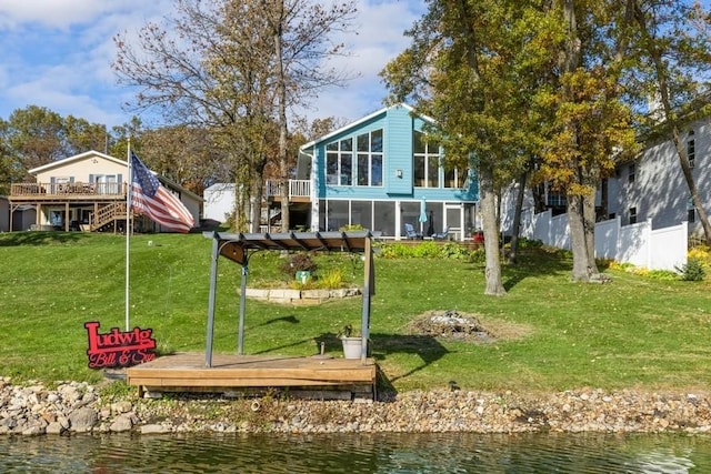 back of house featuring a lawn, fence, a sunroom, a deck with water view, and stairs