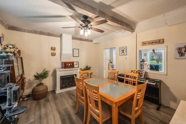 dining area with a glass covered fireplace, dark wood-type flooring, beamed ceiling, and a ceiling fan