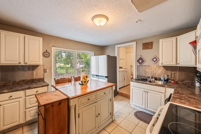 kitchen with electric range, light tile patterned flooring, separate washer and dryer, and a sink