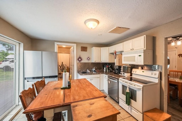 kitchen with a sink, white appliances, light tile patterned flooring, and white cabinetry