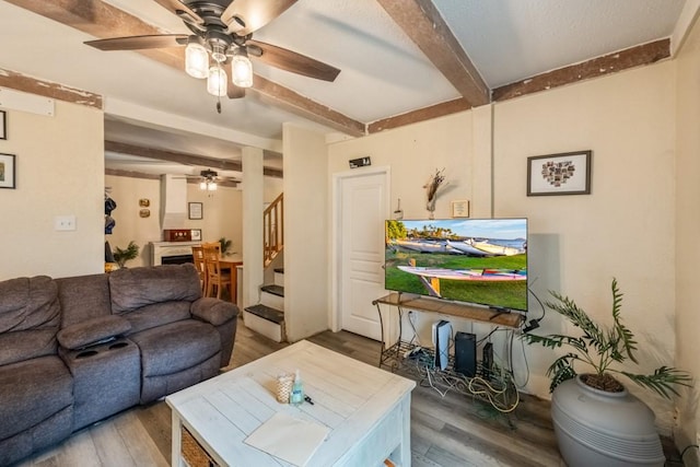 living area featuring beam ceiling, stairway, wood finished floors, and ceiling fan