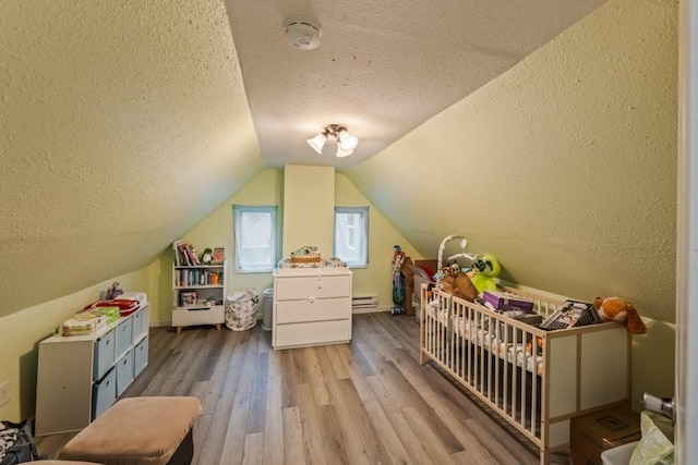 interior space with vaulted ceiling, a textured ceiling, a nursery area, and wood finished floors