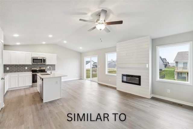 kitchen featuring a fireplace, a sink, stainless steel appliances, vaulted ceiling, and tasteful backsplash