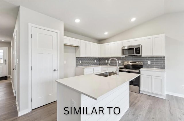 kitchen featuring vaulted ceiling, appliances with stainless steel finishes, light wood-style floors, white cabinets, and a sink