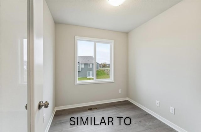 empty room with wood finished floors, visible vents, and baseboards