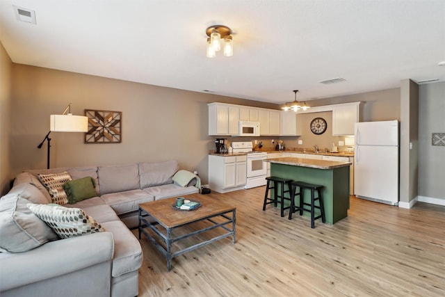 living area with light wood-type flooring, visible vents, baseboards, and an inviting chandelier