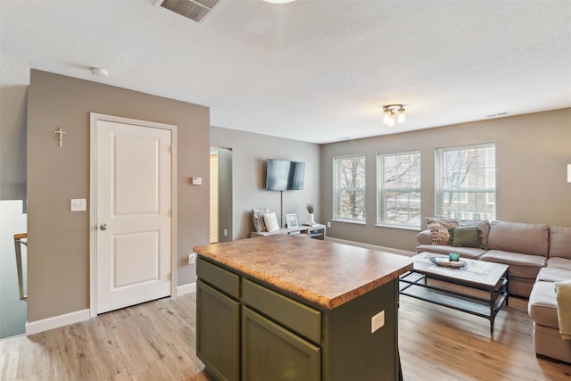 kitchen with baseboards, visible vents, a kitchen island, light wood-type flooring, and open floor plan