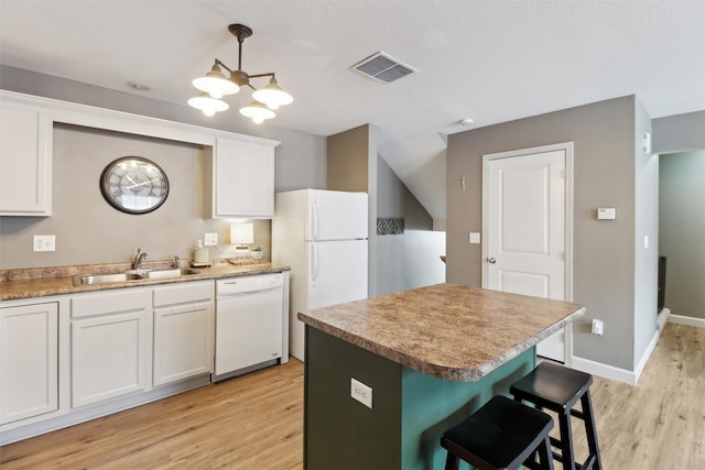 kitchen featuring visible vents, a kitchen bar, light wood-style flooring, a sink, and white appliances