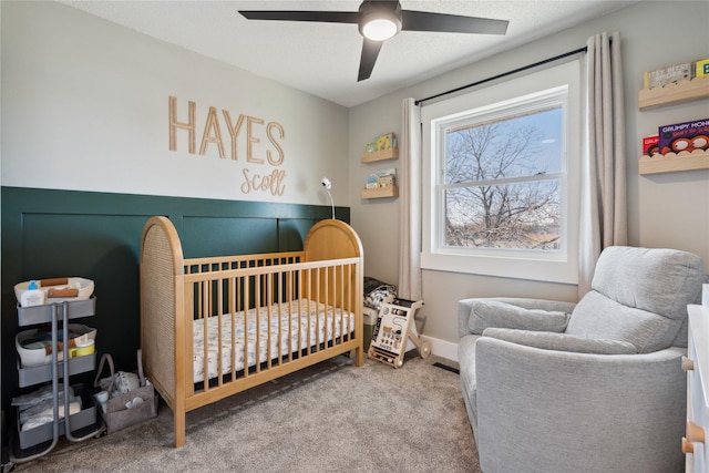 carpeted bedroom featuring a textured ceiling, a crib, and ceiling fan