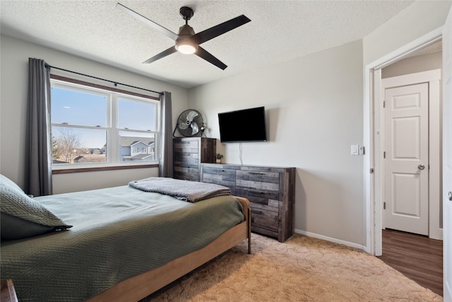 bedroom featuring light colored carpet, a textured ceiling, baseboards, and a ceiling fan