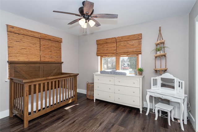 bedroom featuring a crib, dark wood-type flooring, baseboards, and ceiling fan