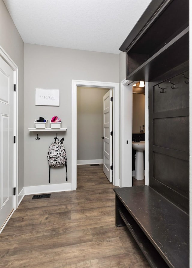 hall featuring visible vents, a sink, baseboards, and wood finished floors