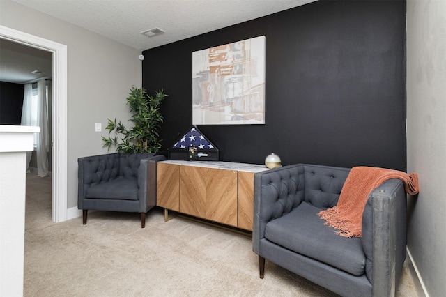 sitting room featuring visible vents, light carpet, a textured ceiling, and baseboards