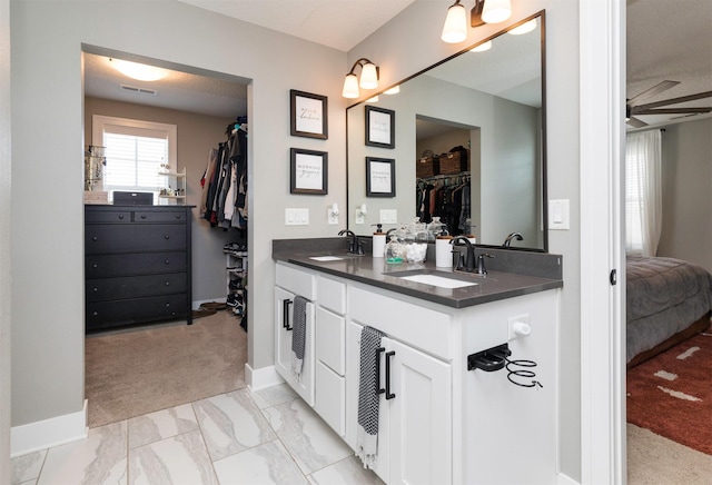 bathroom featuring a walk in closet, double vanity, marble finish floor, and a sink