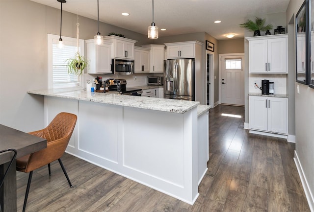 kitchen with light stone counters, dark wood finished floors, a peninsula, stainless steel appliances, and white cabinetry