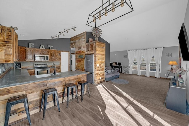 kitchen featuring lofted ceiling, a peninsula, brown cabinetry, stainless steel appliances, and a sink