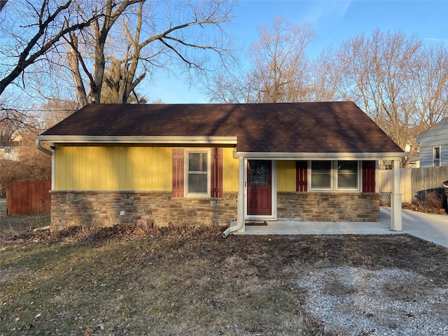 view of front of home with stone siding, a shingled roof, and fence