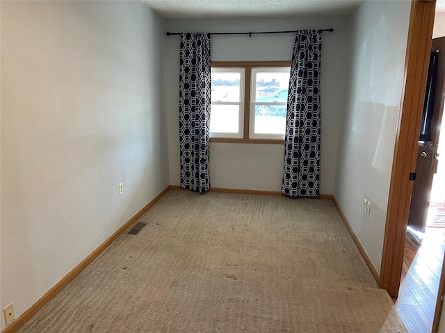 spare room with carpet flooring, visible vents, baseboards, and a textured ceiling