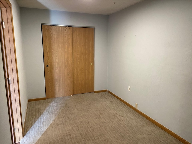 unfurnished bedroom featuring baseboards, a closet, and light carpet