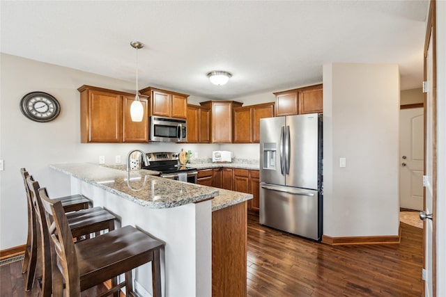 kitchen featuring a kitchen bar, brown cabinets, dark wood-type flooring, stainless steel appliances, and a peninsula