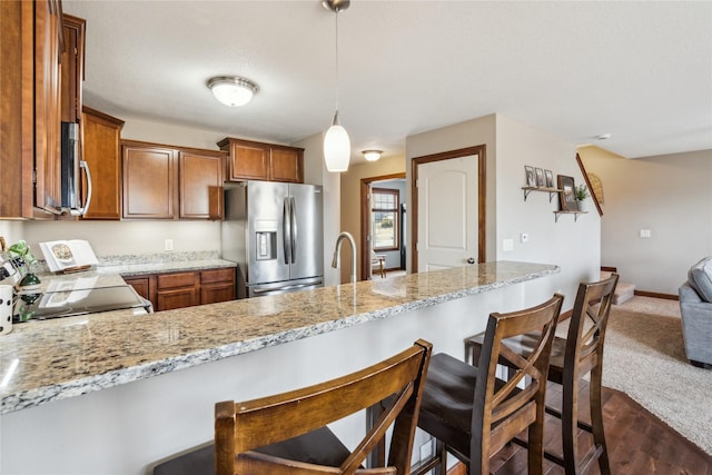 kitchen featuring light stone countertops, a breakfast bar, a peninsula, stainless steel appliances, and brown cabinets