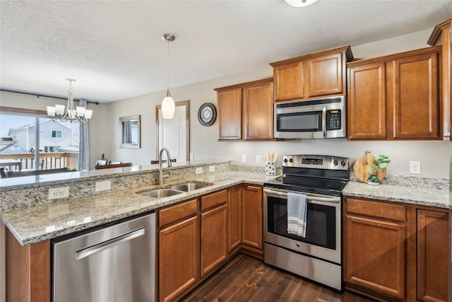 kitchen with a peninsula, a sink, dark wood-type flooring, appliances with stainless steel finishes, and brown cabinets